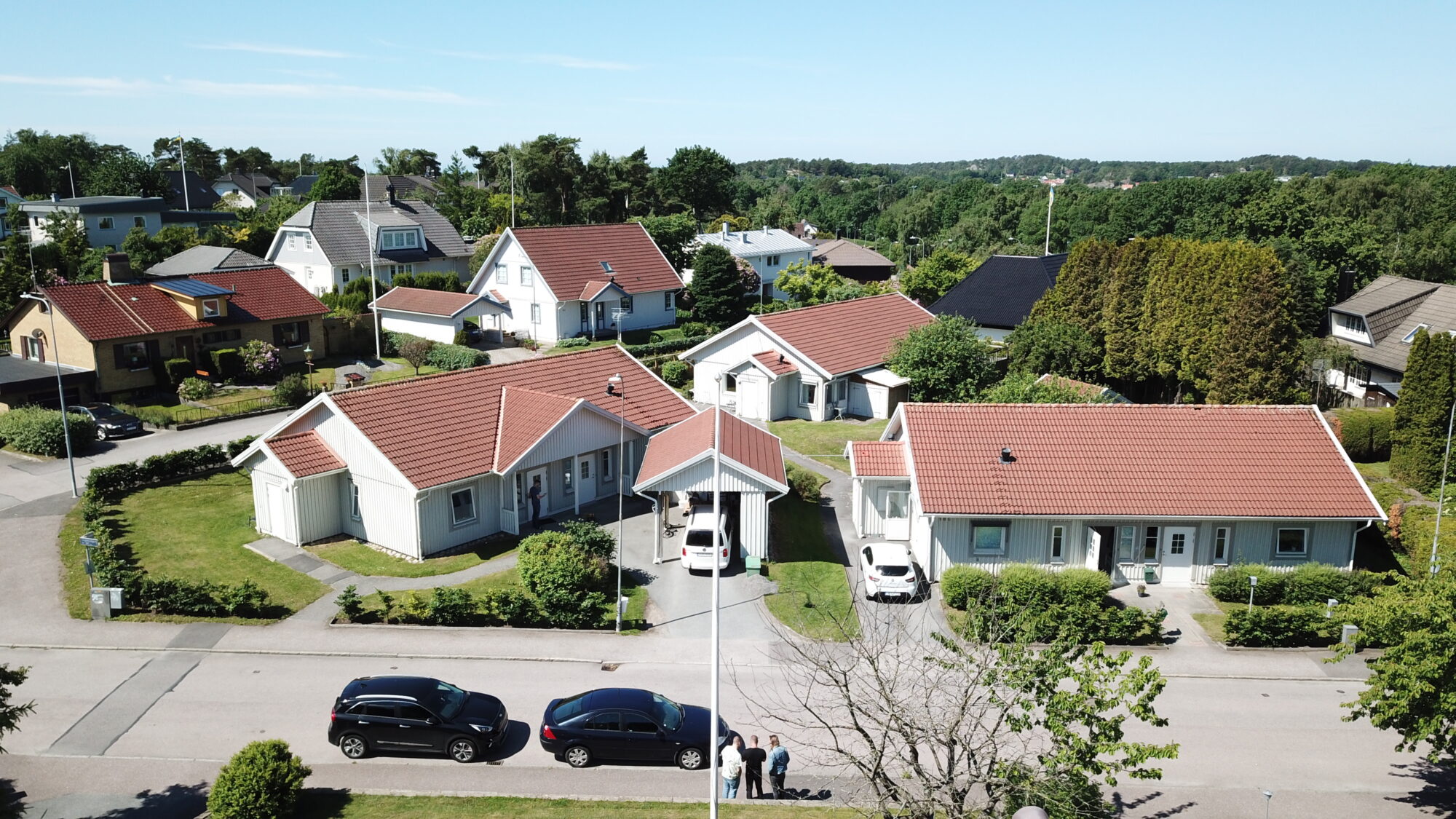 Lingonvägens gruppbostad, flygvy över tre vita hus med röda tak med trädgård och parkering