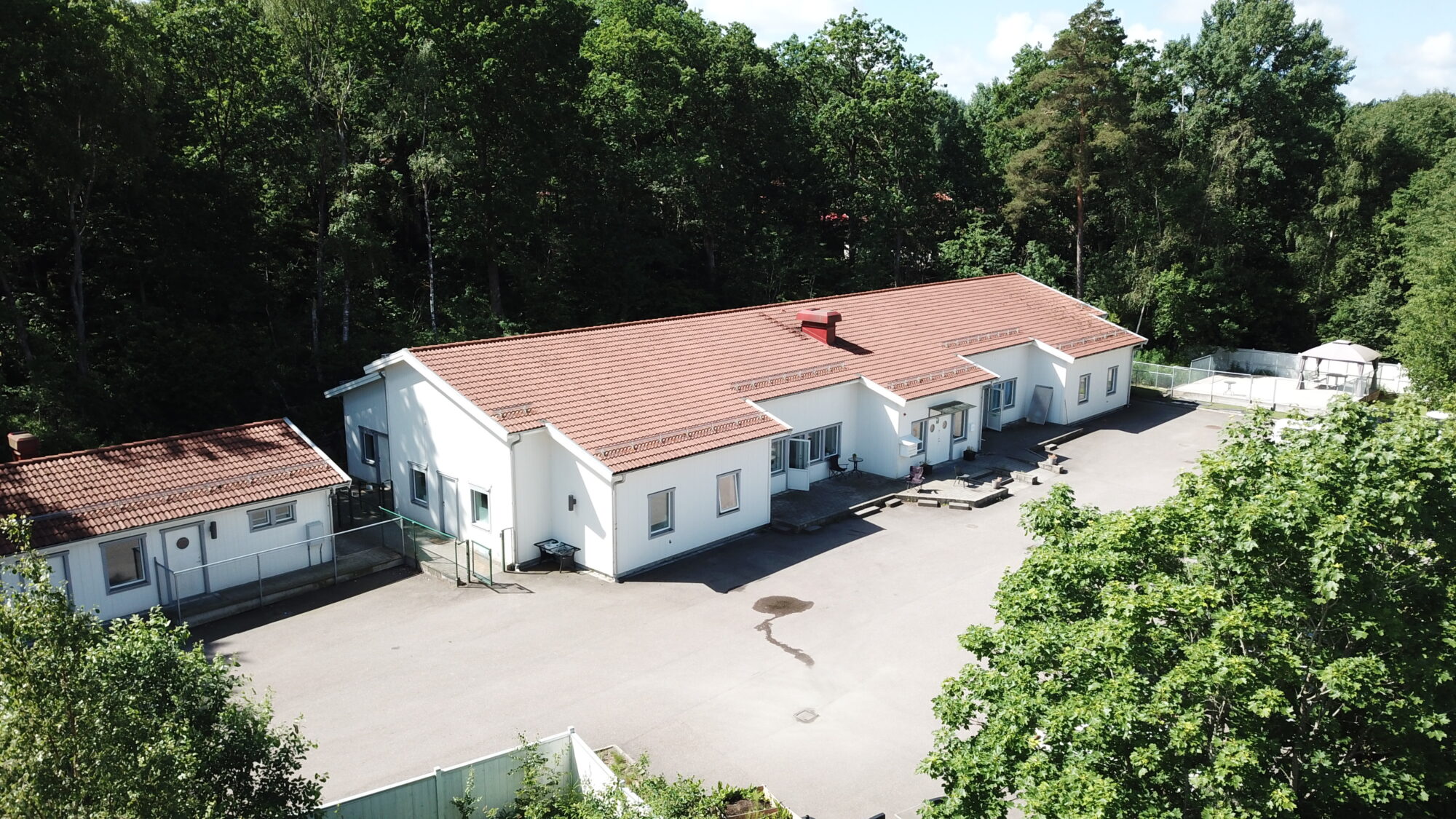 Kvarnens gruppbostad,flygvy över lång vit byggnad vid skogskant med gårdsplan