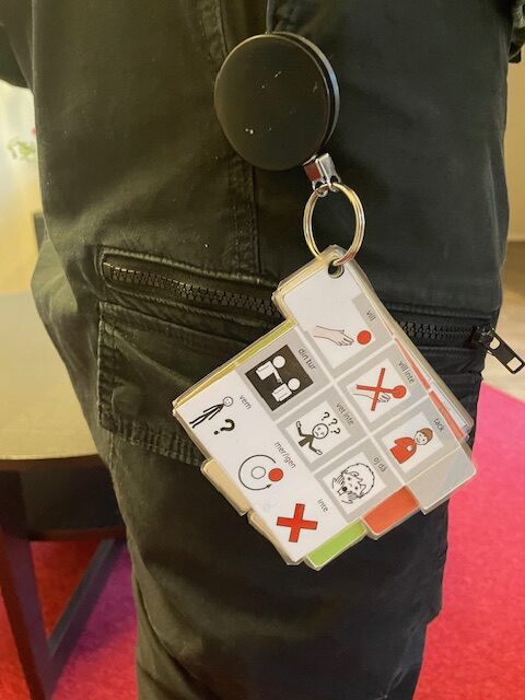 Närbild på en persons midja med mörka byxor och en nyckelring fastsatt i bältet. I nyckelringen sitter laminerade bilder med symboler, en sk.samtalsknippa.