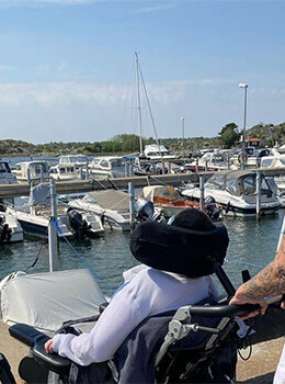Person i rullstol som tittar ut över havet och bryggor där båtar ligger förtöjda.
