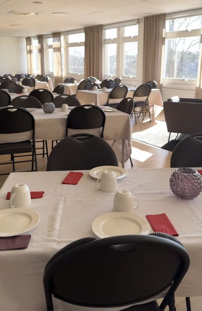 Stora konferensrummet Havet med flera dukade bord och svarta stolar,ljus från stora fönster längs väggen och porslin uppställt på borden.