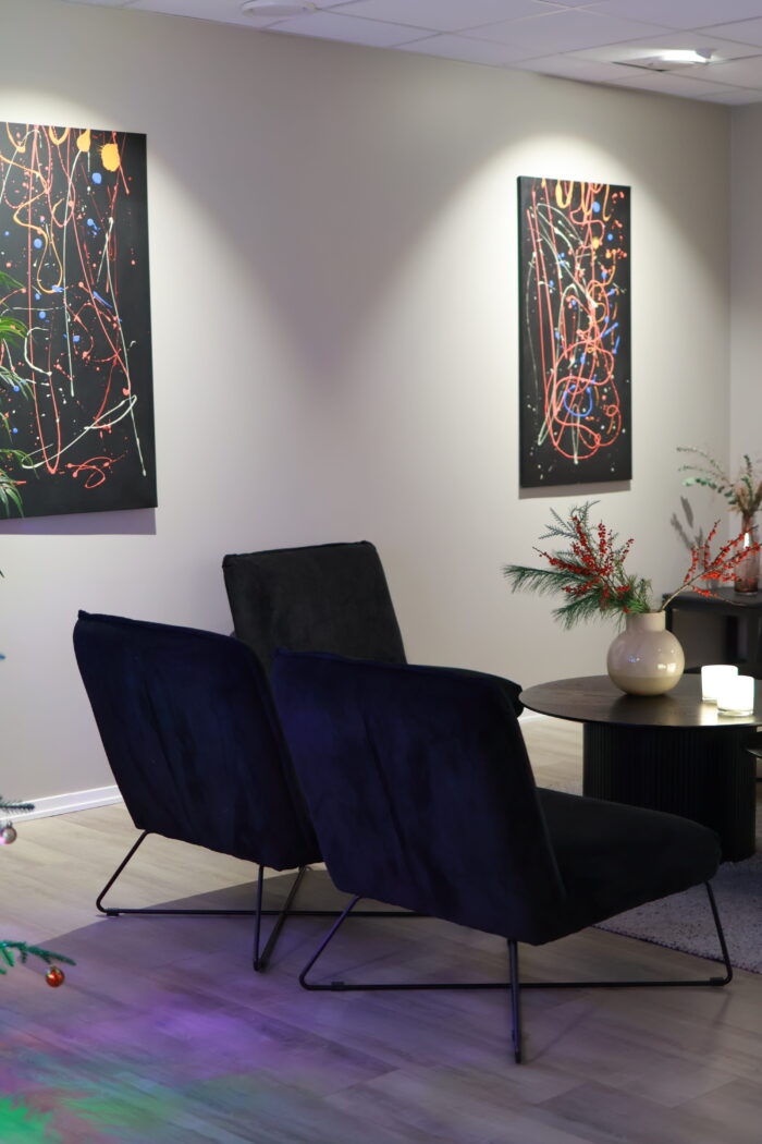 Mysigt hörn i ett rum med två mörka fåtöljer, litet sidebord med blomarrangemang och två färgstarka tavlor på väggen ovanför.