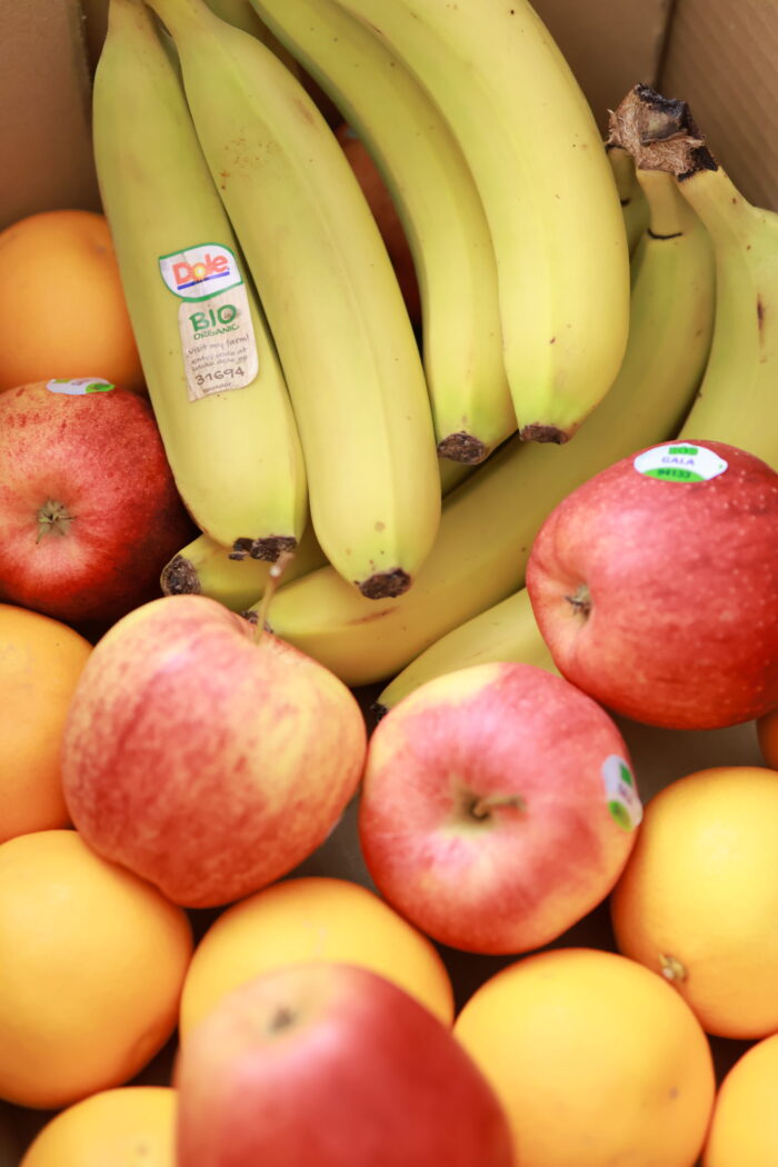 Närbild av fruktkorg med gula bananer och röda äpplen samt citrusfrukter tätt placerade tillsammans.