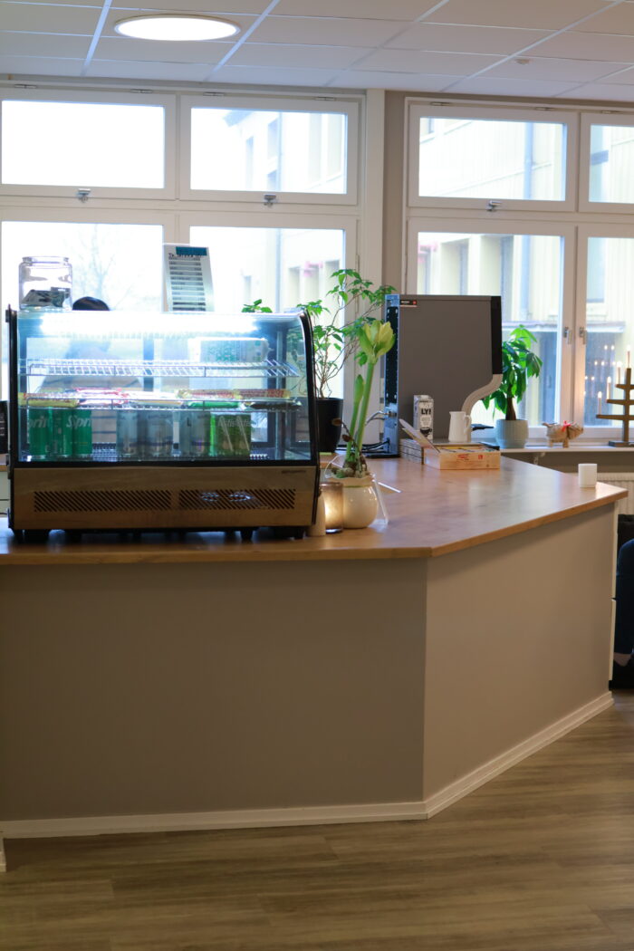 Serveringsdisk i ljust rum med stora fönster, växter och utrustning för dryck eller servering på bänken.