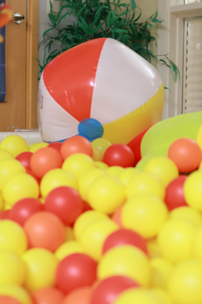 Ett bollhav fyllt med gula och röda plastbollar. En stor randig badboll ligger ovanpå. Inomhusmiljö med sinnesstimulerande utrustning.