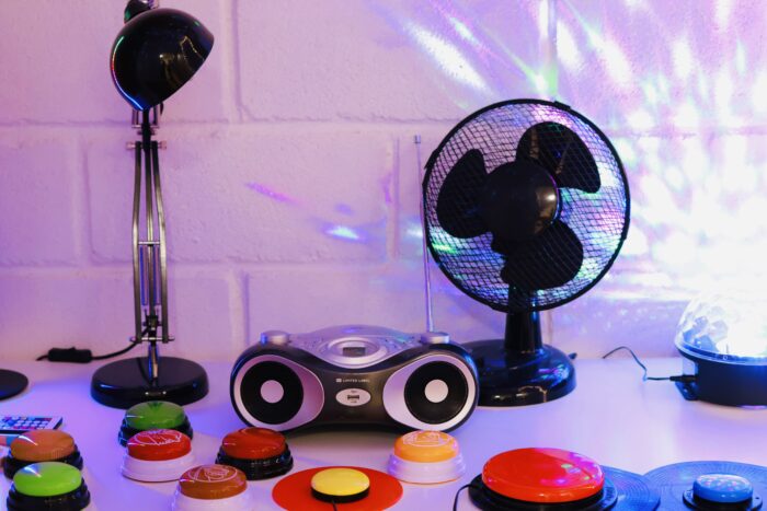 En arbetsbänk med färgglada knappar i olika storlekar. Mot väggen på bänken står en skrivbordslampa, en cd-spelare, en fläkt och en discolampa.
