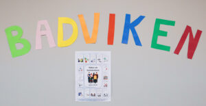 En banner visas med färgglada bokstäver som stavar BADVIKEN med stora bokstäver