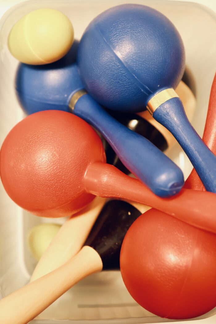 Närbild på färgglada rytminstrument,bland annat maracas och klubbor i blått,rött och gult,samlade i en behållare.