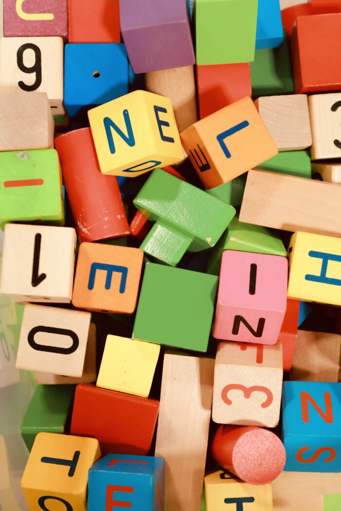 Närbild av en hög med färgglada träklossar och bokstavsklossar med siffror och bokstäver i blandade färger och former.