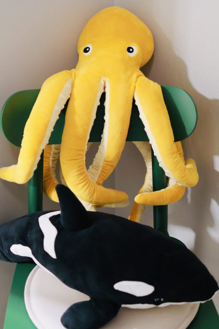 En gul bläckfiskfigur och en svartvit späckhuggare i mjukt material sitter på en grön stol. Sinnesstimulerande föremål i ett rum.