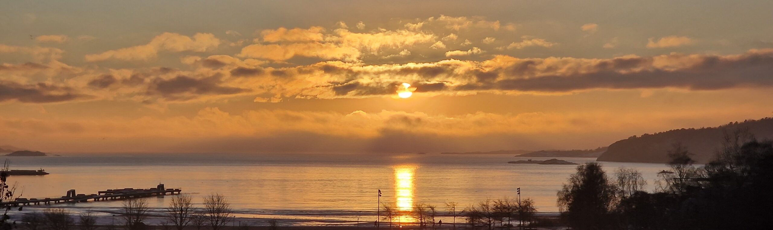 Solnedgång över blankt hav. Ett band av moln går över himlen.