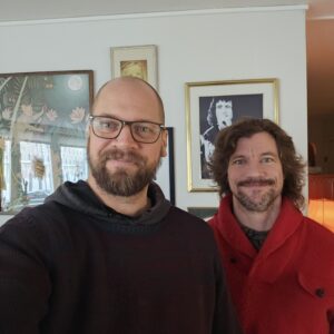 Bild på Henrik och Tomas som leder podden. De är klädda i röd och svart tröja mot en vägg prydd av tavlor.