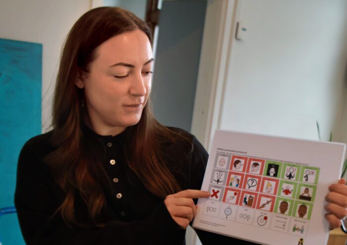 En kvinna sitter inomhus, håller upp och pekar på ett bildschema.