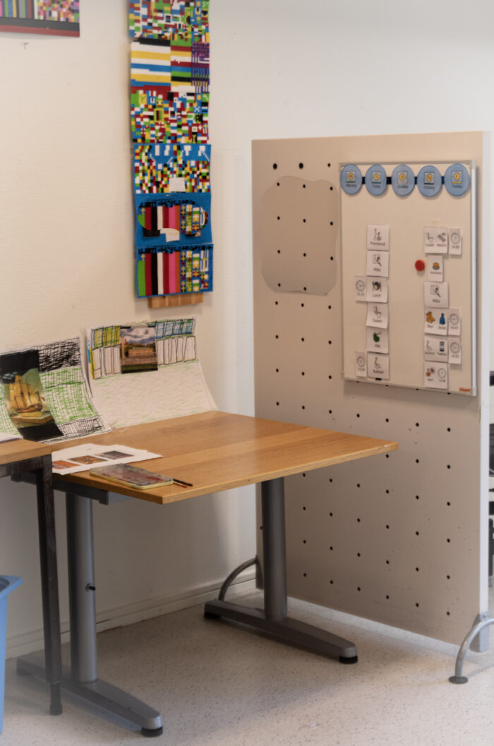 Ett arbetsbord i ett aktivitetsrum med material på bordet. På väggen bakom sitter färgglada hyllor och ett planeringsschema.