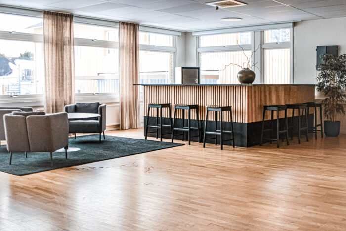 Bar med träpanel och svarta pallar. till vänster i bild ser man en grupp med svarta fåtöljer på en grå matta.