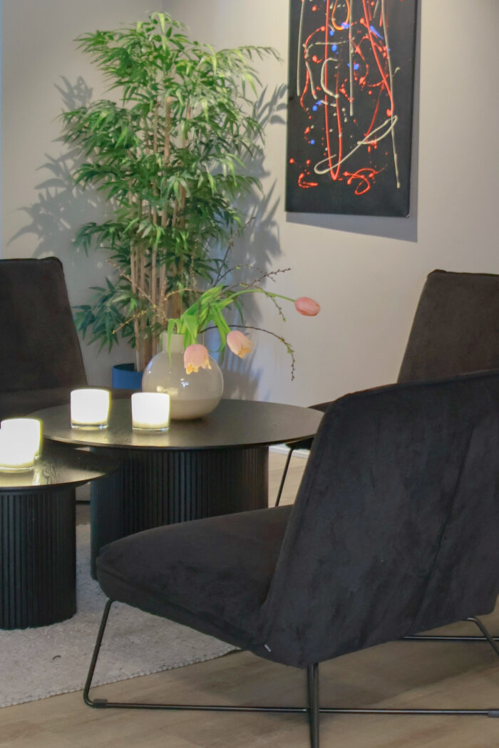 Loungegrupp med svarta fåtöljer och två svarta runda bord. En stor grön växt bakom gruppen.