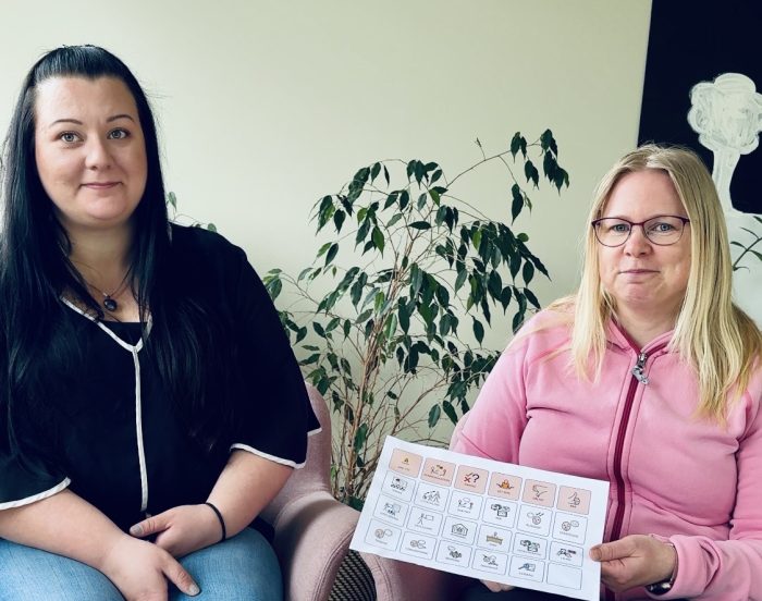 Två personer tittar mot kameran. Den ena har en samtalskarta i handen