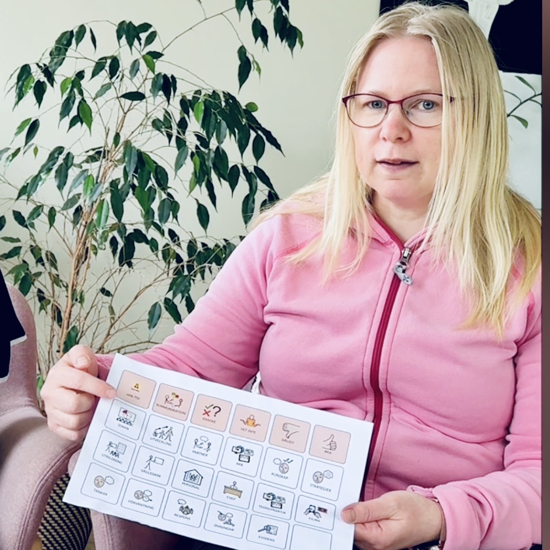 Person i rosa luvtröja sitter i fåtölj med en samtalskarta i handen.